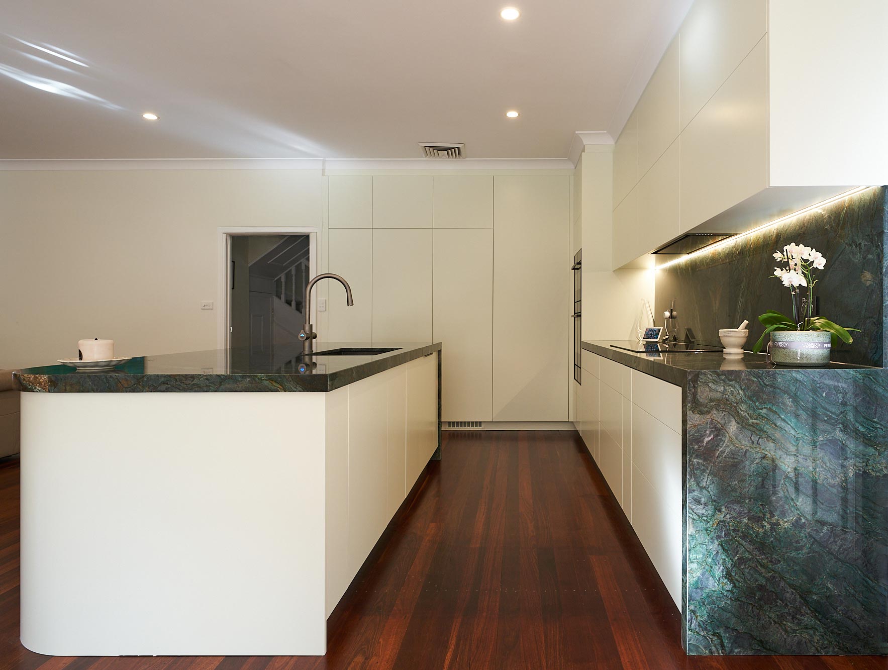 Flat white kitchen with green stone waterfall island by Renolux